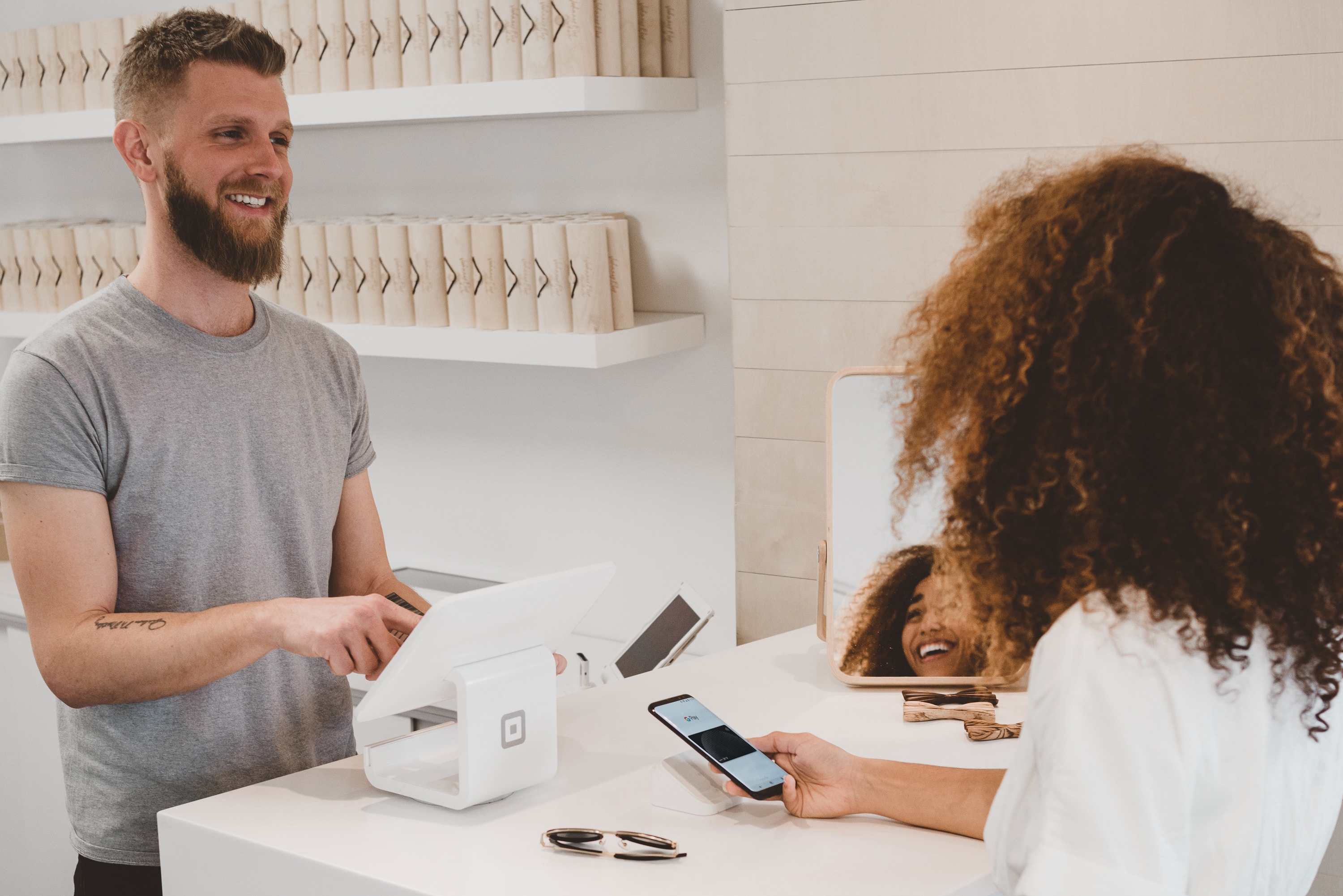 Customer smiling and paying with her phone to a man.