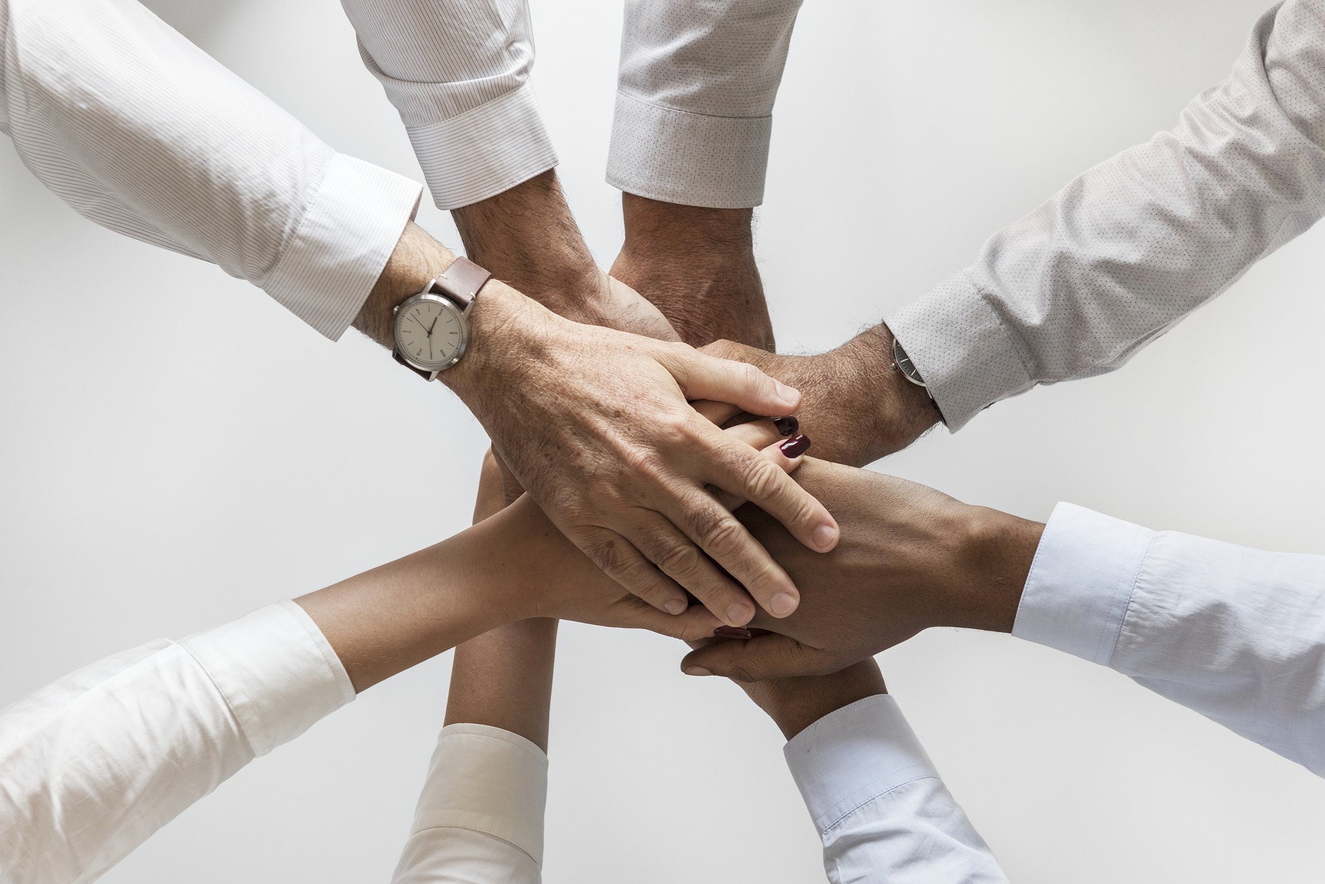 multiculturalism: a group of office workers with different skin tones placing their hands on top of one another