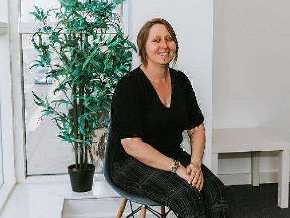 Image of Alex-Michelle Parr, Managing Director of Wolfestone Group, pictured in an office. Alex is sat on a stool, looking towards the camera with a green tree behind her on the windowsill.