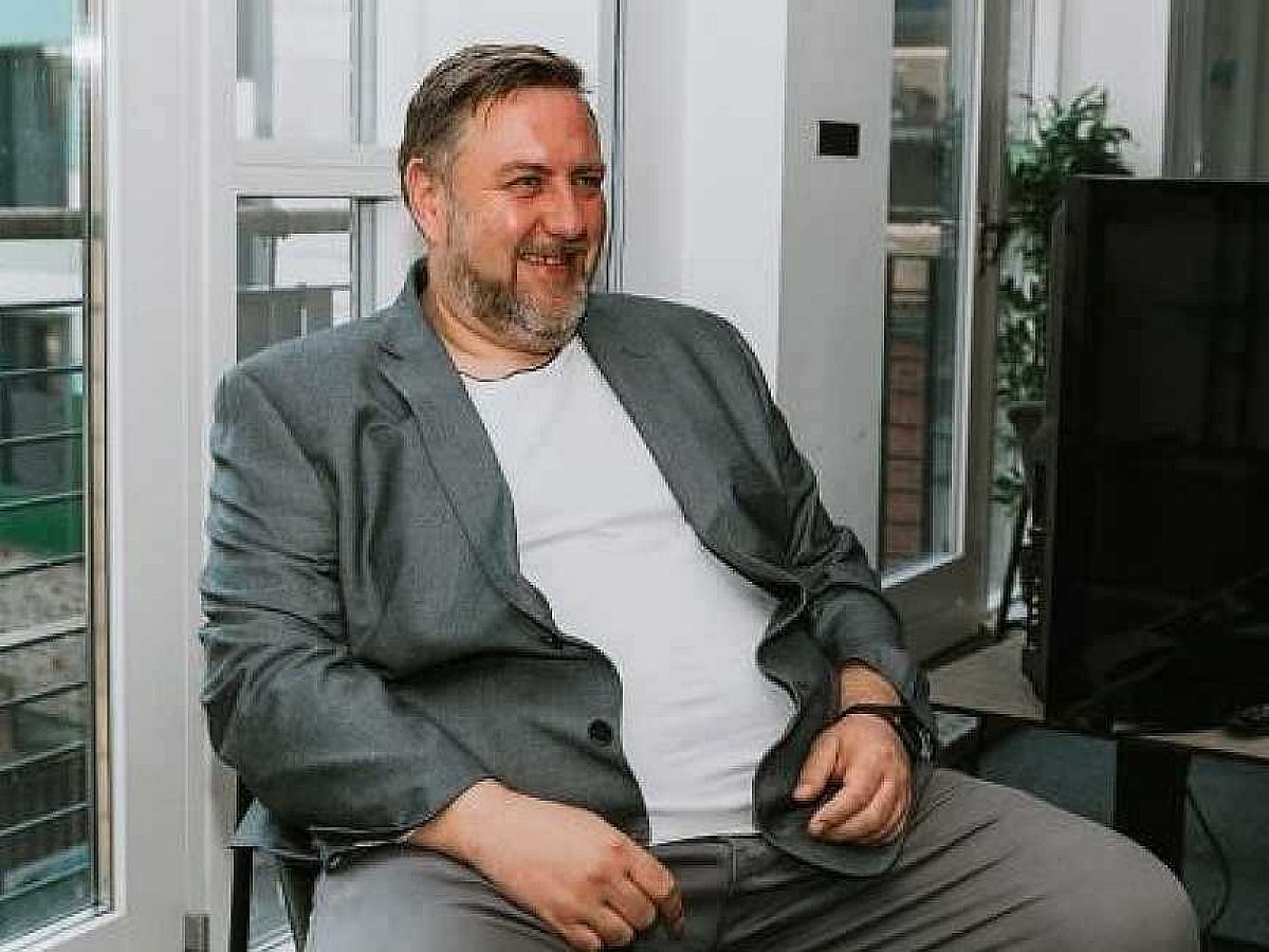 Wolfestone’s Chief Technology Officer, Norbert Pietrzak, is sat on a chair smiling away from the camera wearing a grey suit jacket and pants