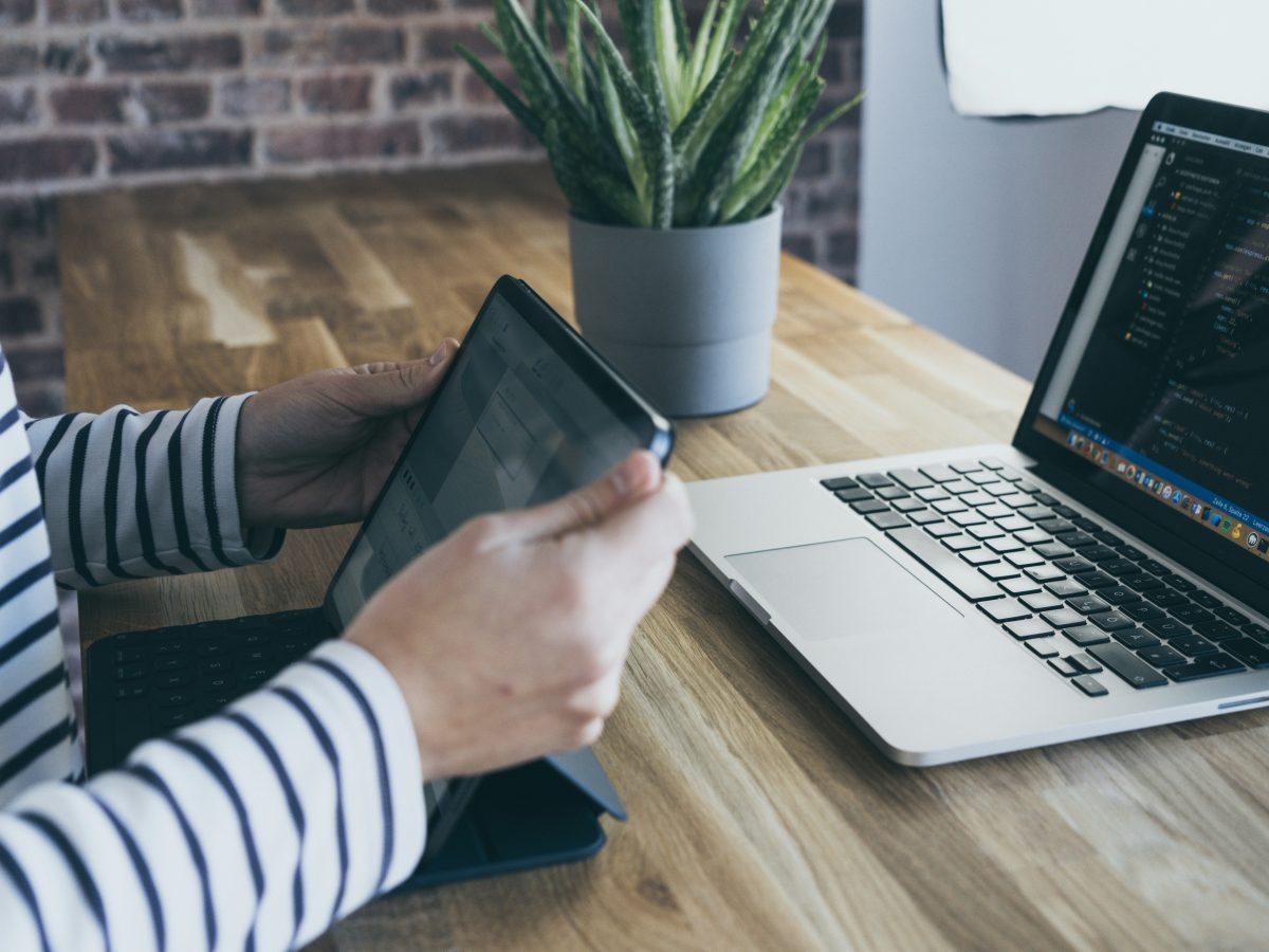 A person is using a tablet with their laptop behind on the table