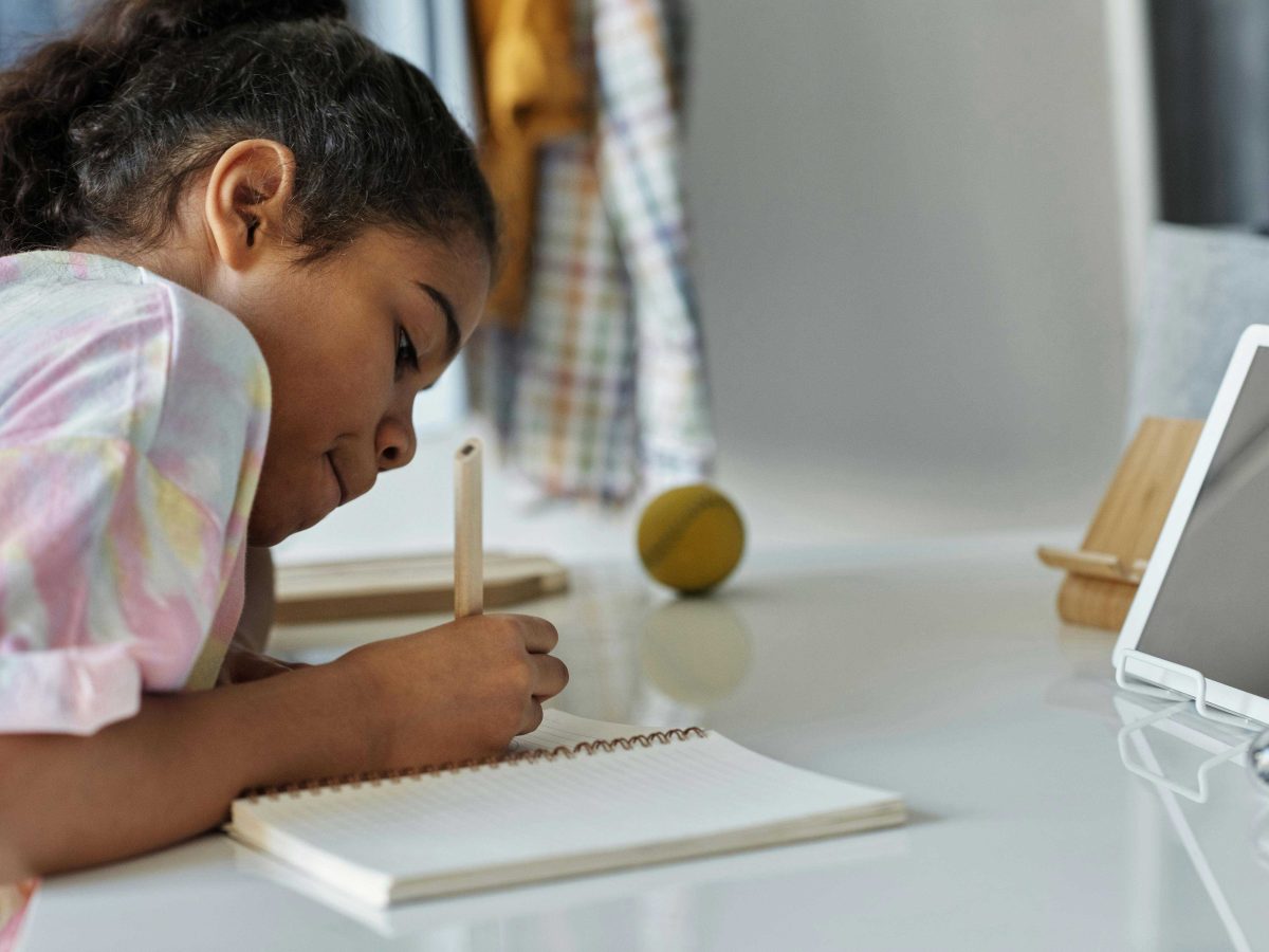 A young girl is writing on white paper with a screen setup in front of her