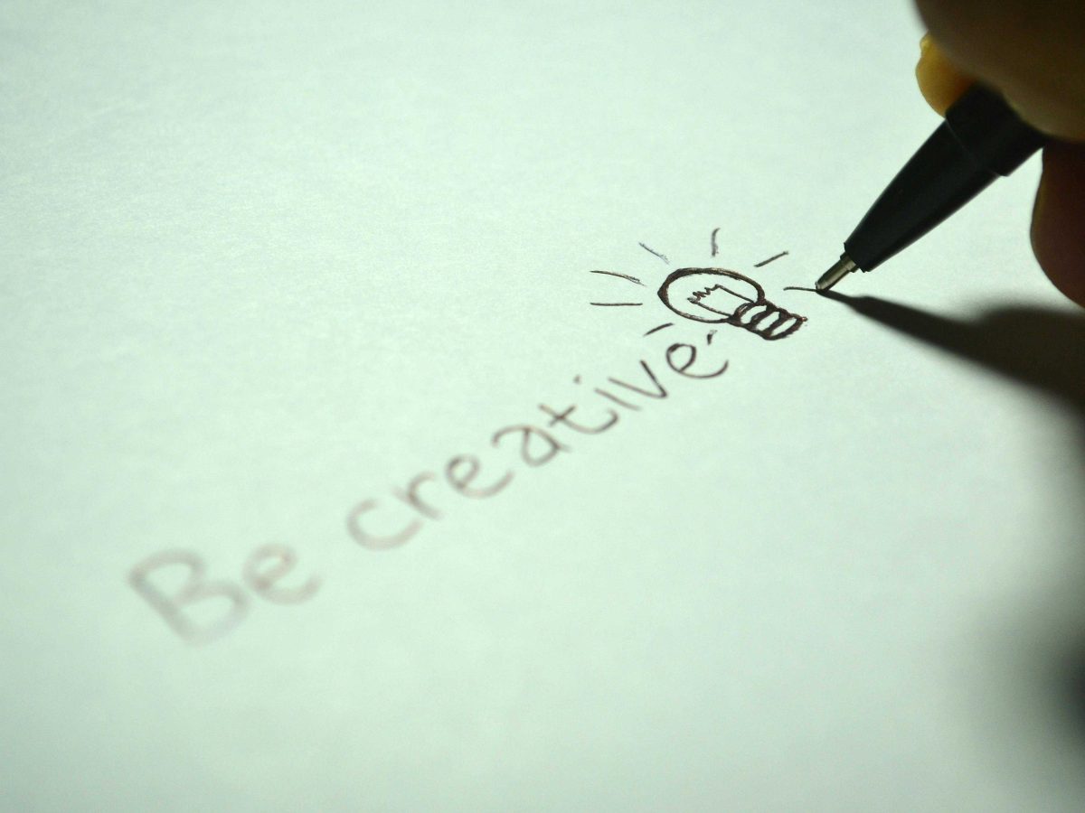 Person writing "Be Creative" on paper
